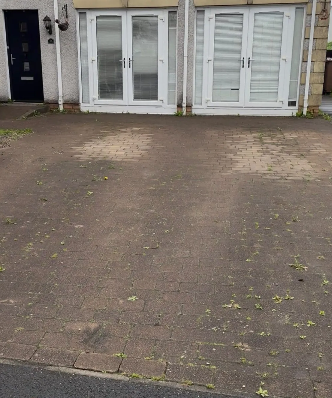 Block paving driveway in front of French doors, dark with grime and weeds before cleaning