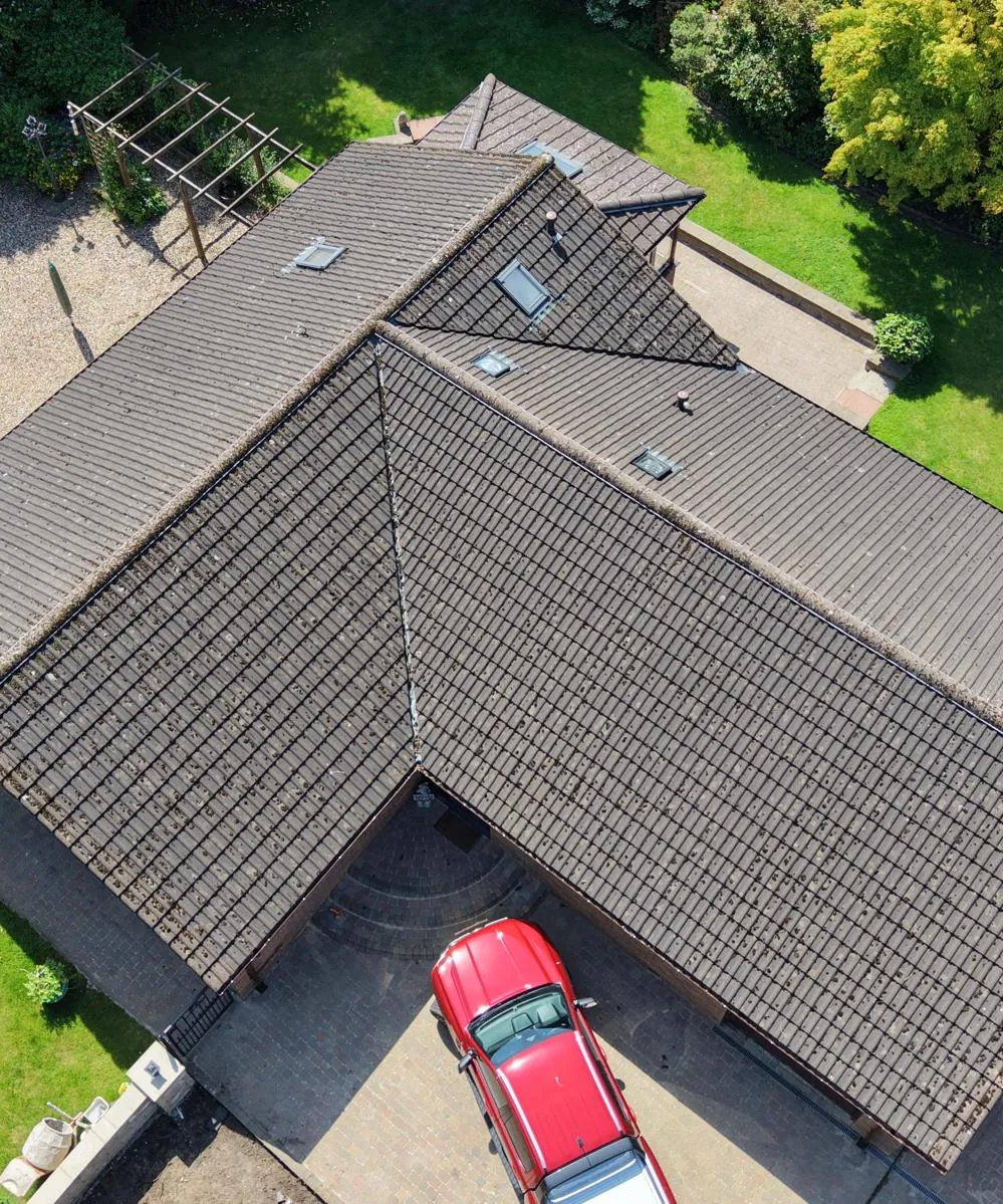 Aerial view of a concrete tile bungalow roof covered in dark moss before cleaning